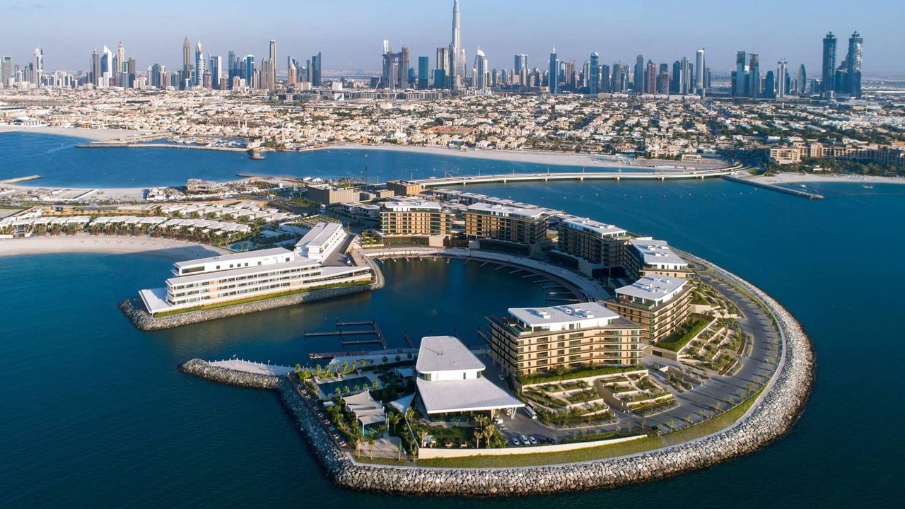 An aerial view of Jumeirah Bay Island and the city of Dubai behind it, including a view of the Burj Khalifa
